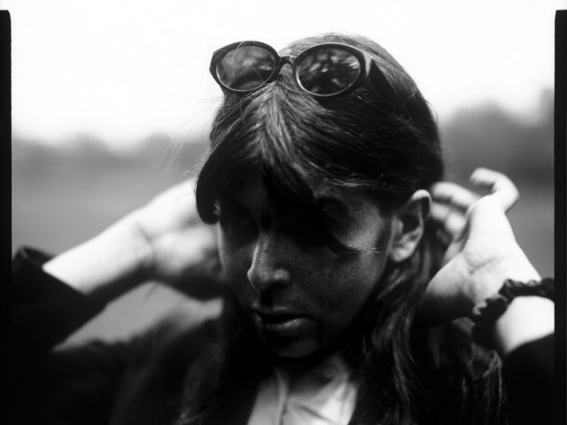 This is a black and white photograph of a person in a park putting their hair behind their ears.