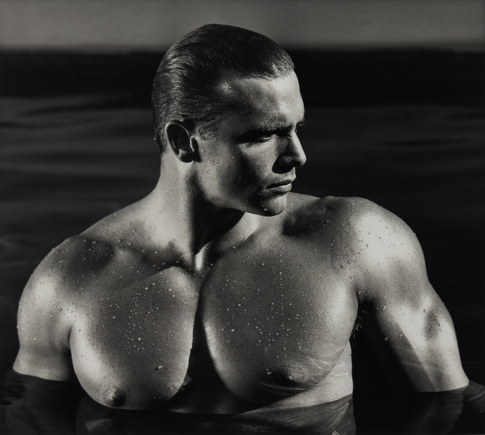 This is a black-and-white photograph of a handsome shirtless man in water.