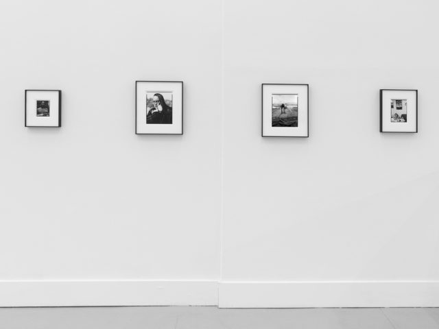 This is a photograph of black and white framed images on display in a minimalistic gallery setting.