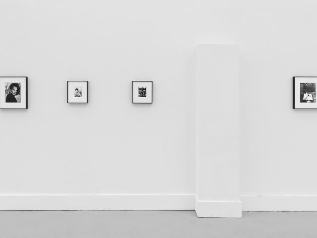 This is a photograph of black and white framed images on display in a minimalistic gallery setting.