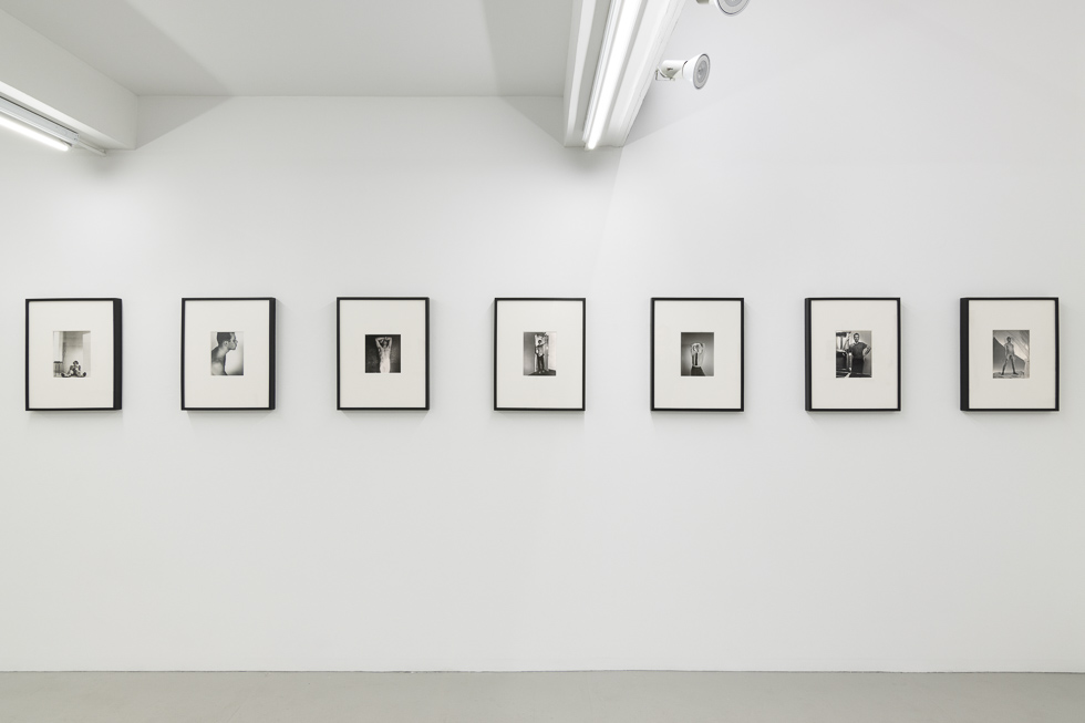 This is a photograph of black and white photographs installed in a white-walled gallery setting.