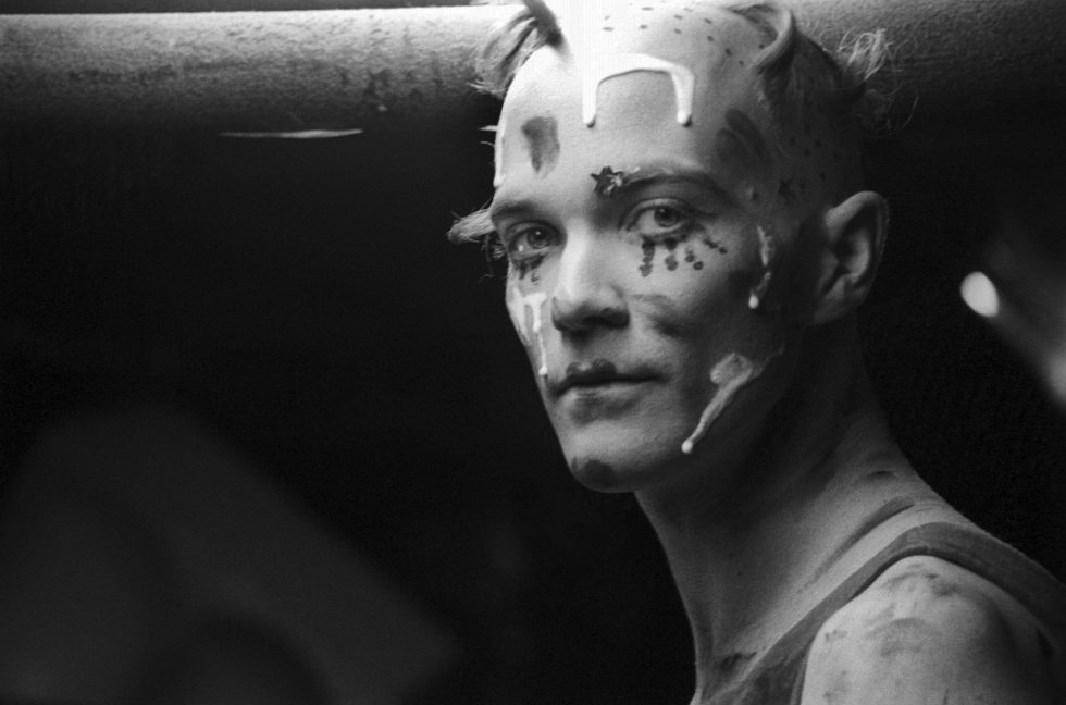 This is a black and white portrait of a man wearing face paint.