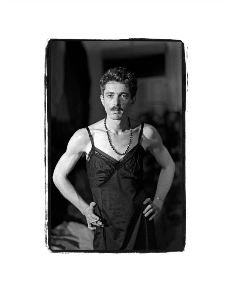 This is a black and white photograph of a man in a black dress with his hands on him hips.