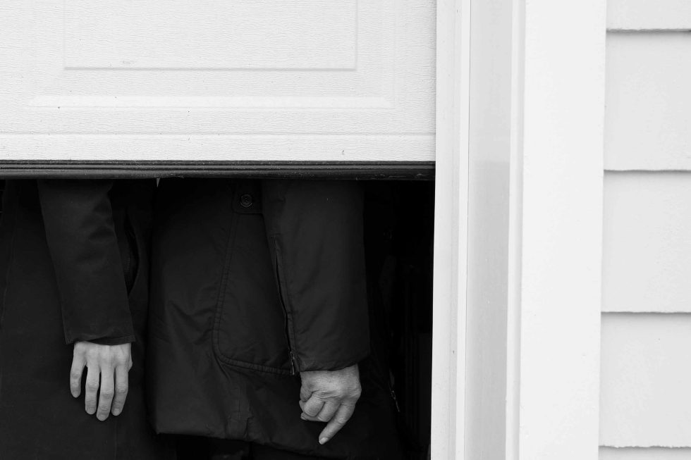 This is a black and white photograph of two hands below a garage door.