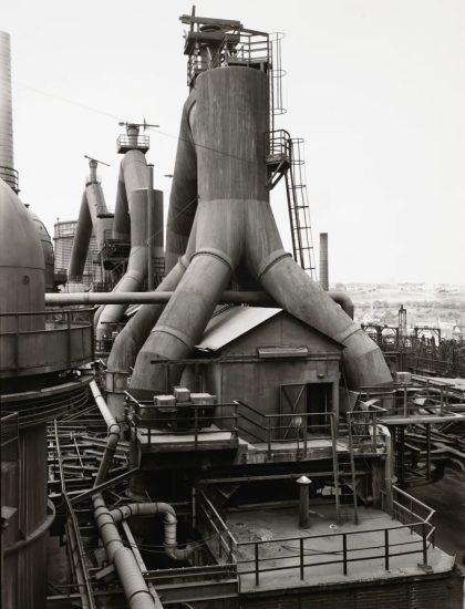 This is a black-and-white photo of an industrial steel mill with towering blast furnaces and complex piping.