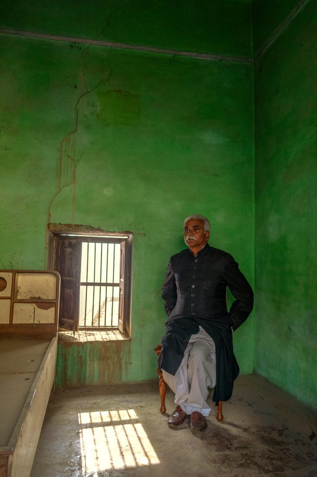 This is a photograph of a man in an empty room next to a green wall.