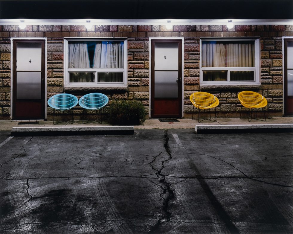 This is a color photograph of an entrance to a motel with colorful chairs in front.
