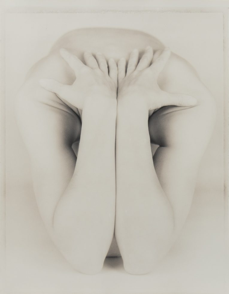 This is a black and white photograph of a nude woman's hands and arms on her shoulders.