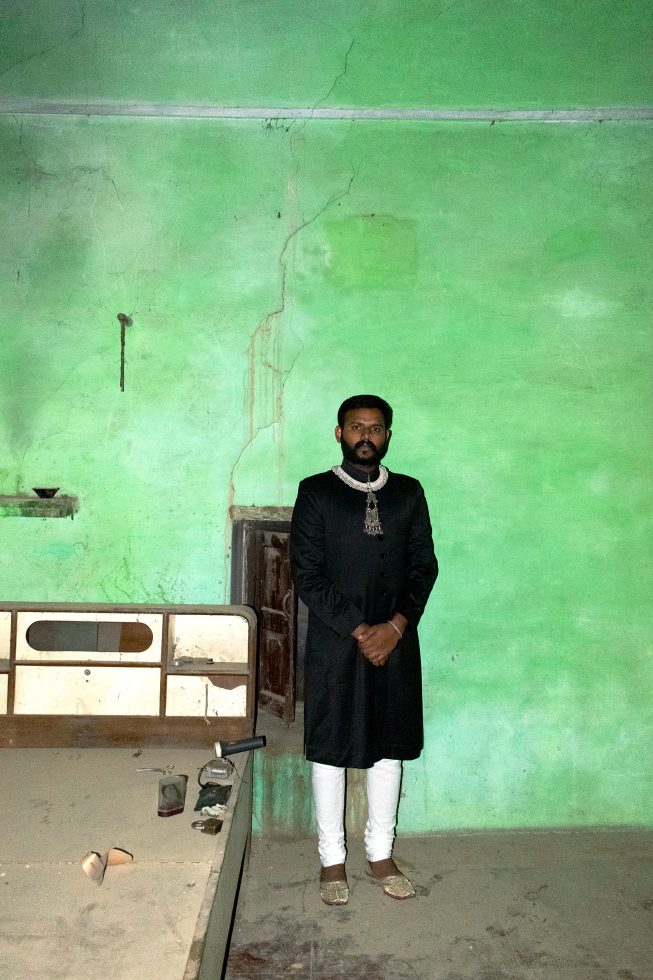This is a color photograph of a man standing in a green room.