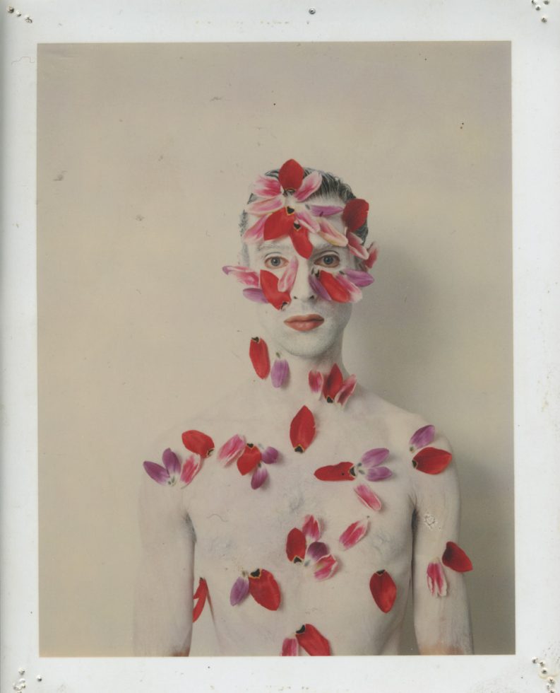 This is a photograph of a man covered in red flower petals.