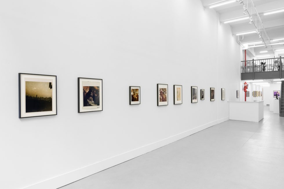This is a photograph of a series of pictures hanging on the wall of a white, stark, gallery space.