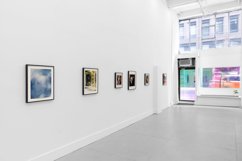 This is a photograph of a series of pictures hanging on the wall of a white, stark, gallery space.
