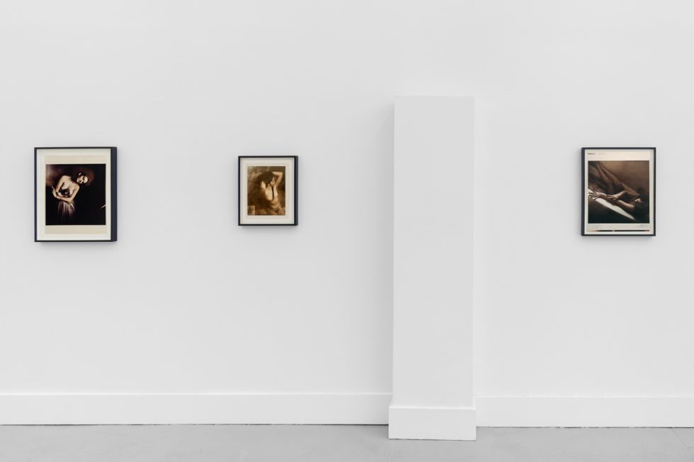This is a photograph of a series of pictures hanging on the wall of a white, stark, gallery space.