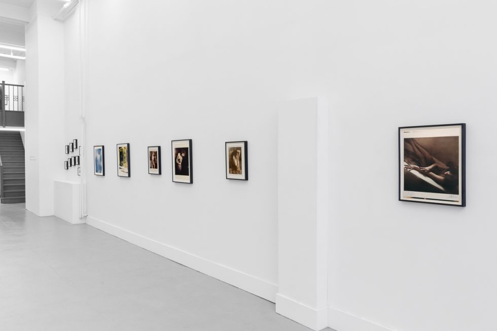 This is a photograph of a series of pictures hanging on the wall of a white, stark, gallery space.