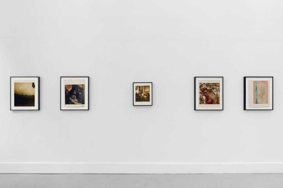 This is a photograph of a series of pictures hanging on the wall of a white, stark, gallery space.