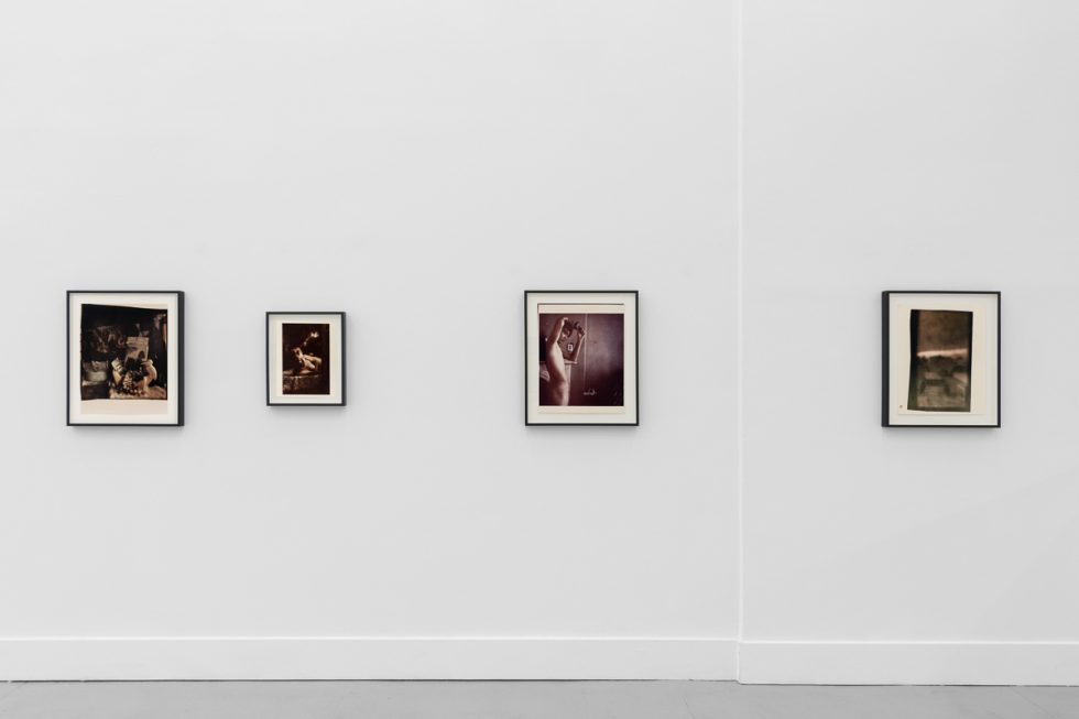 This is a photograph of a series of pictures hanging on the wall of a white, stark, gallery space.
