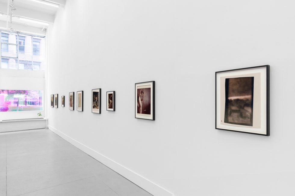 This is a photograph of a series of pictures hanging on the wall of a white, stark, gallery space.