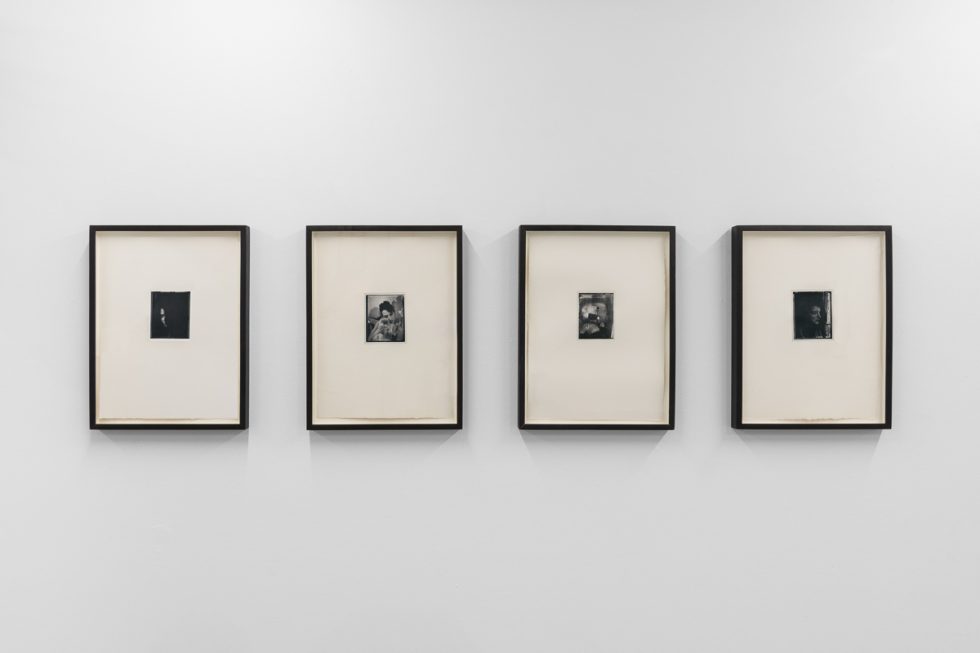 This is a photograph of a series of pictures hanging on the wall of a white, stark, gallery space.