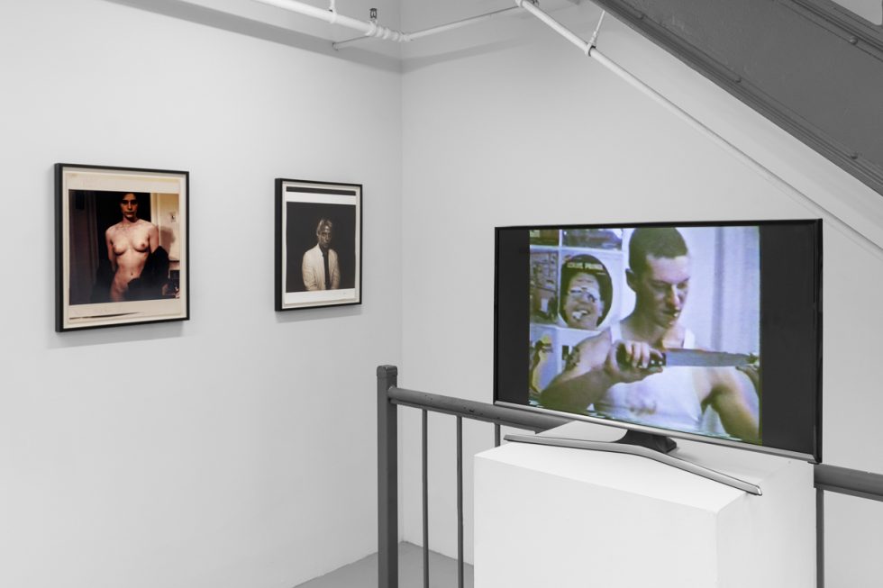 This is a photograph of a series of pictures hanging on the wall of a white, stark, gallery space.