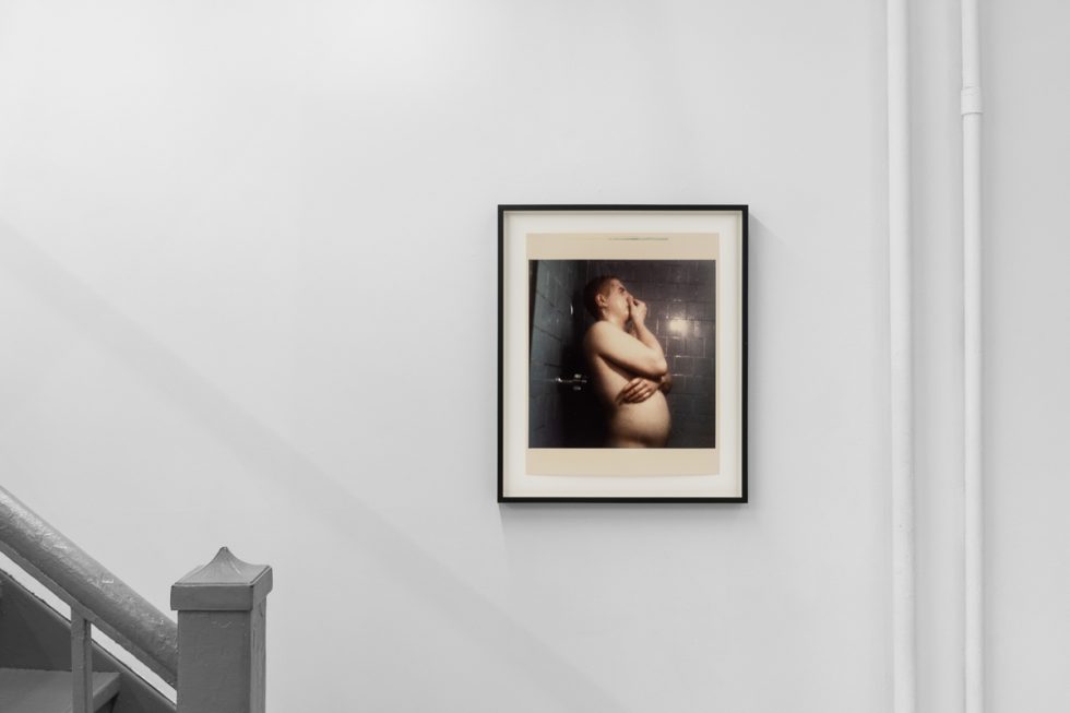This is a photograph of a series of pictures hanging on the wall of a white, stark, gallery space.
