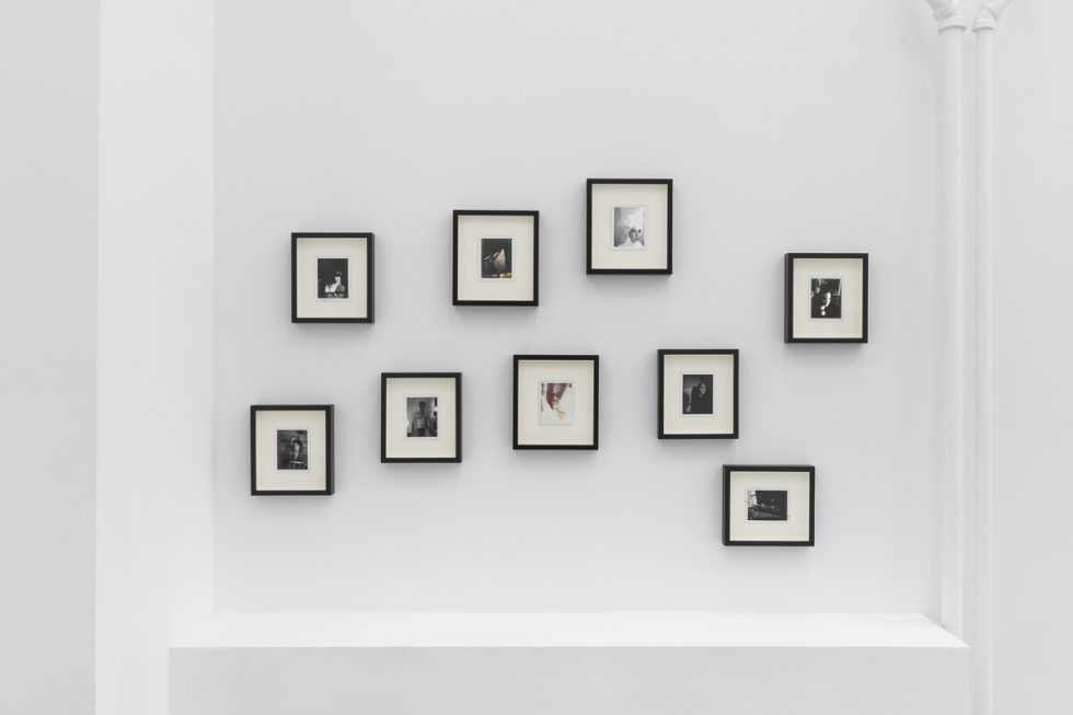 This is a photograph of a series of pictures hanging on the wall of a white, stark, gallery space.