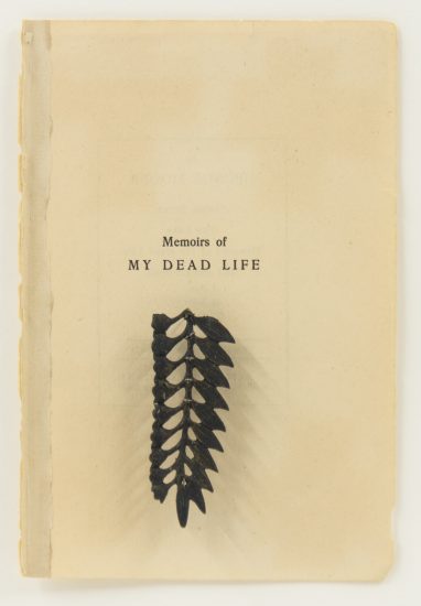 Click for sizes / editions / prices. The image shows an old, worn page titled Memoirs of My Dead Life. Below the title is a small, black botanical element, resembling a pressed or carved leaf or fern, attached to the page.