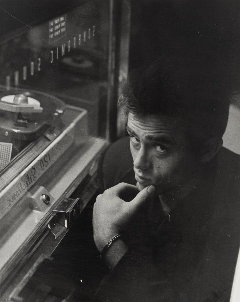A black and white photograph of a handsome man holding his chin next to a jukebox.