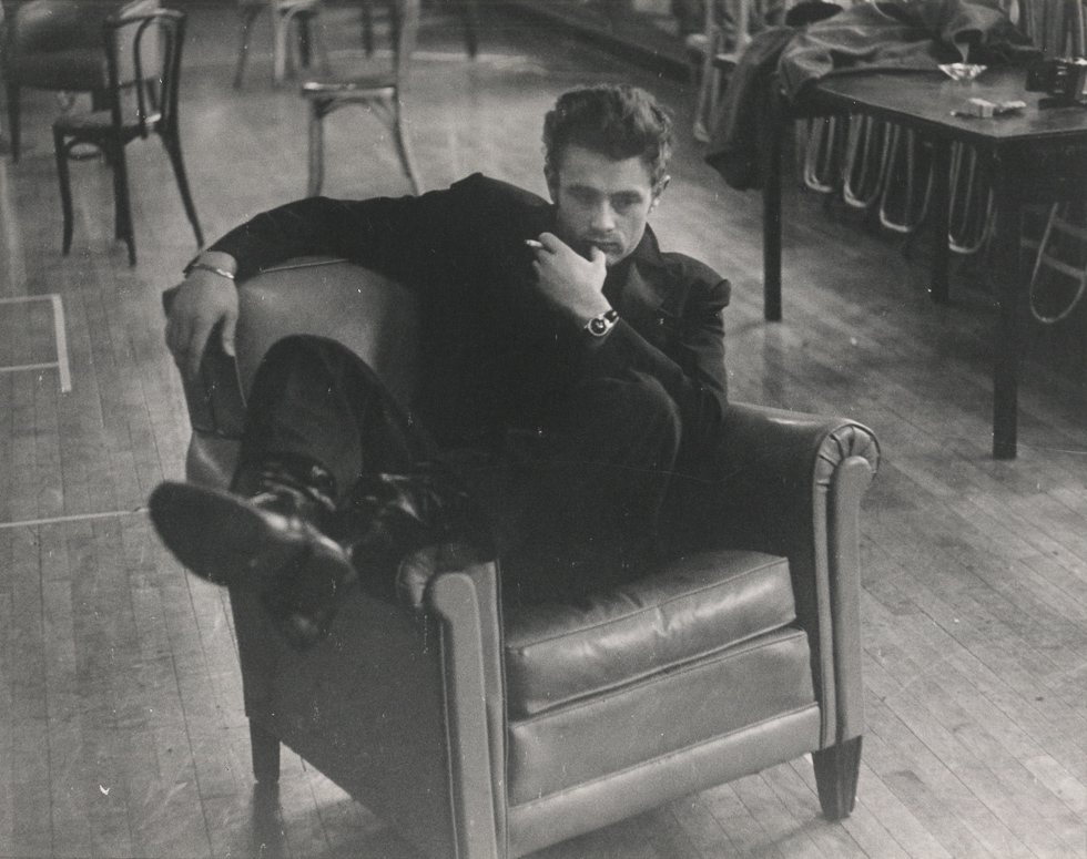 A black and white photograph of a handsome man sitting in a leather chair holding a cigarette.