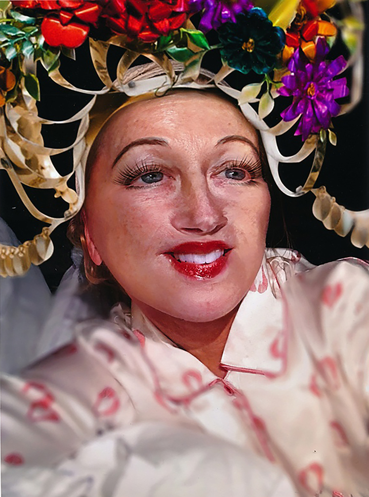 A headpiece and exaggerated prosthetic facial features create a jarring and unsettling effect.