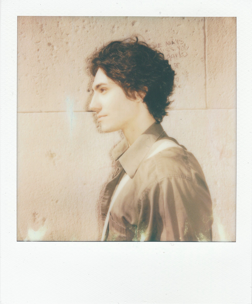 A polaroid of a young man in profile with dark hair against a stone wall.