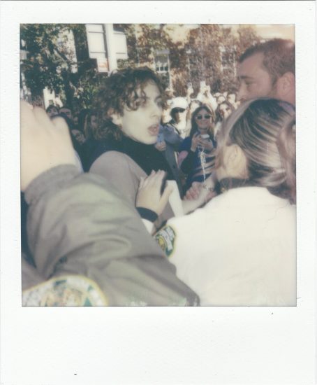 Click for sizes / editions / prices. A polaroid of a group of people in a crowd with a young man with curly dark hair in the center of the scene.