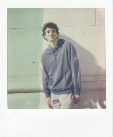 Click for sizes / editions / prices. A polaroid photograph of a young man in a grey hoodie against a stone wall.