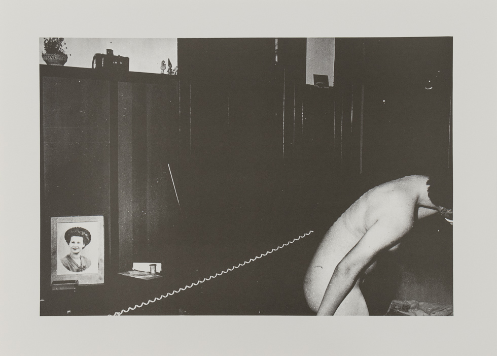 A nude figure leans over while holding a phone connected to a cord