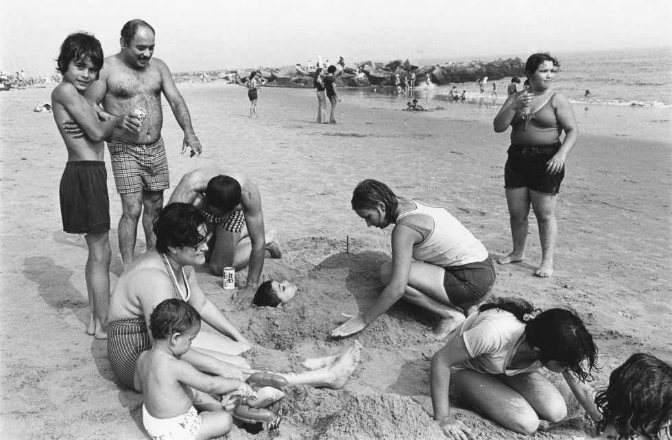 A black and white photograph of a family playing on a sandy beach.