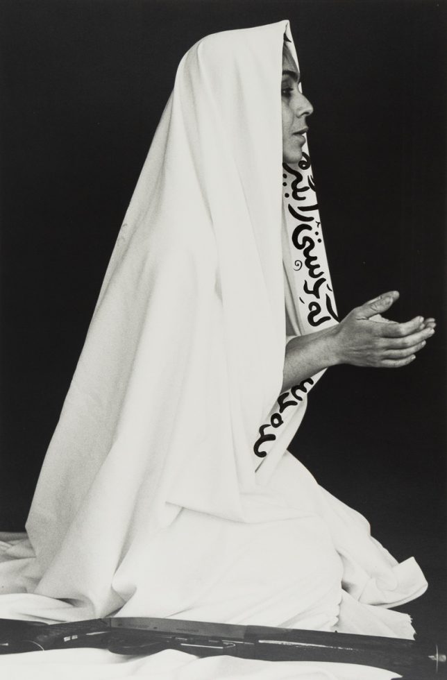 A black and white photograph of a woman in a white cloth with her hands together in prayer.