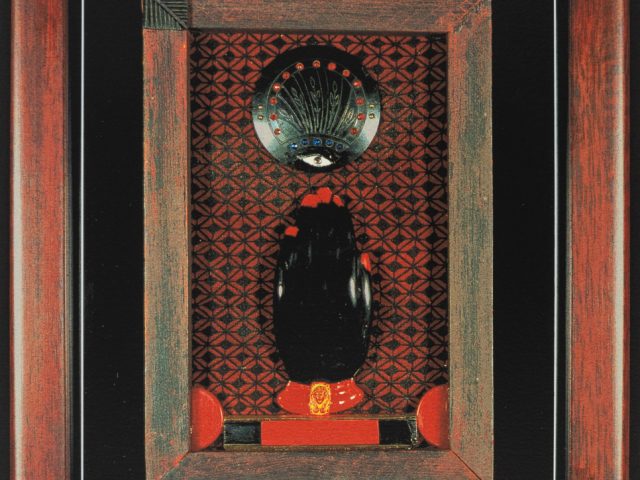 A mixed-media assemblage by Betye Saar featuring a totemic black form, a mystical eye motif, and geometric patterns within a rustic wooden frame.