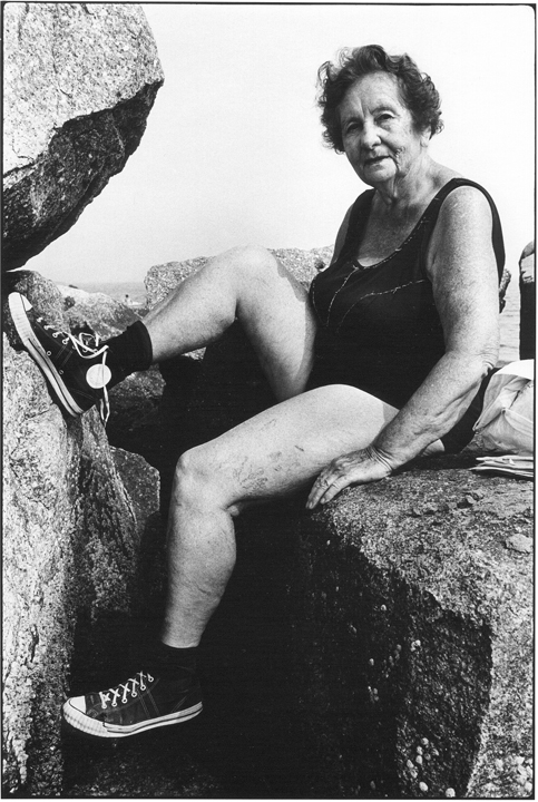 A black and white photograph of a woman wearing sneakers sitting on a rock.