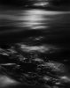 A dark seascape with shimmering light reflecting on the water and rocky shoreline in a soft, ethereal glow.