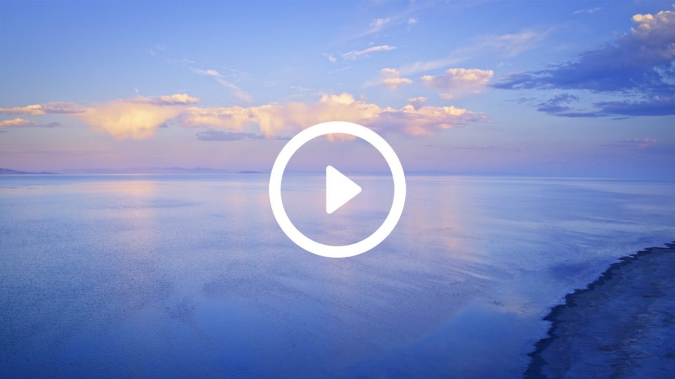 A tranquil lake reflects the soft hues of dawn with golden clouds stretching across the sky.