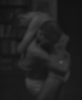 Two partially clothed figures embrace in a dark, blurry setting with indistinct background elements.