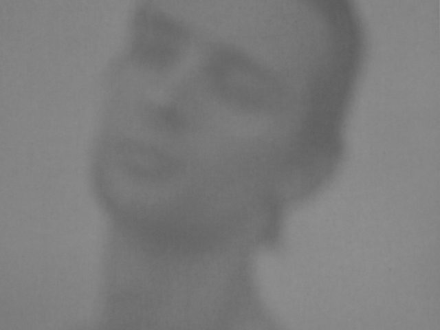 A blurry black and white image of a young man's face.