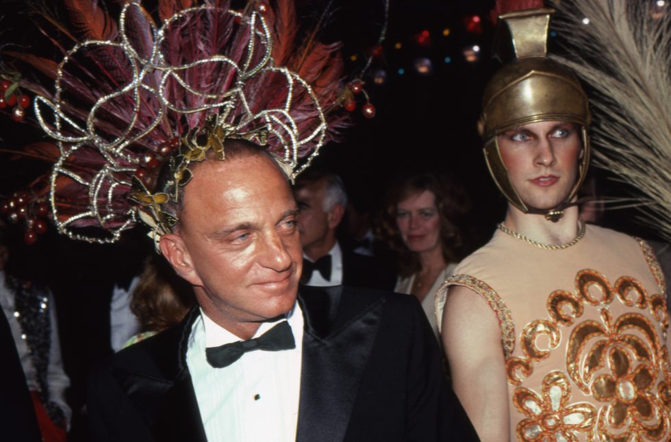 A color photograph of an old man in a tuxedo next to a flamboyant young man in gladiator costume.