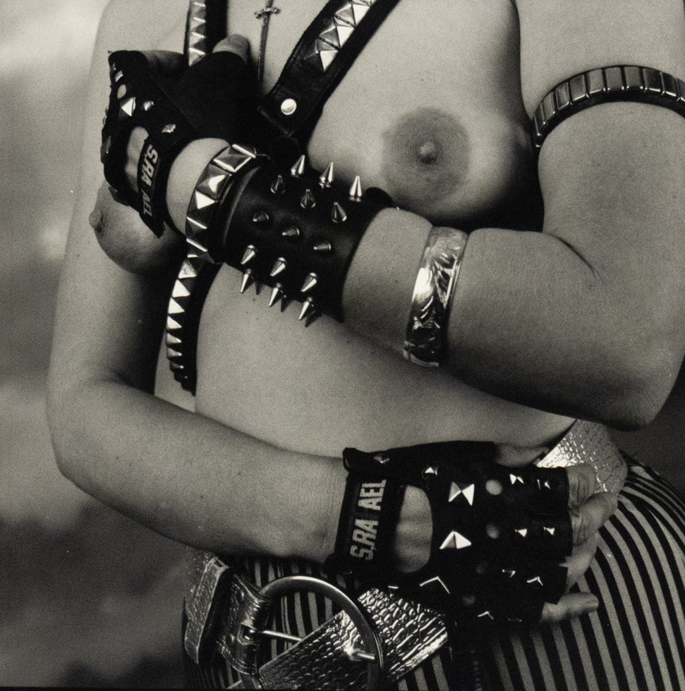 A black and white photograph of a nude person in leather gear.