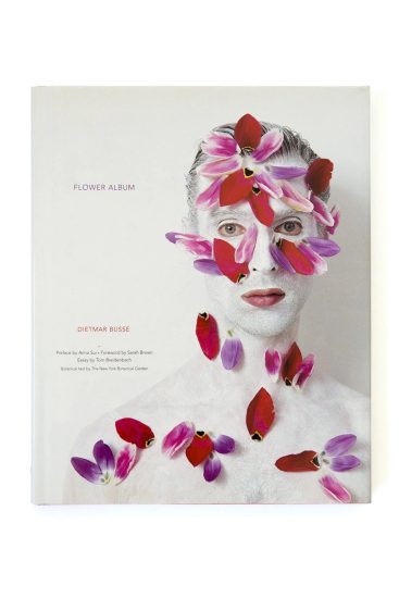 A photograph of a man in white paint with flower petals on his face and torso  