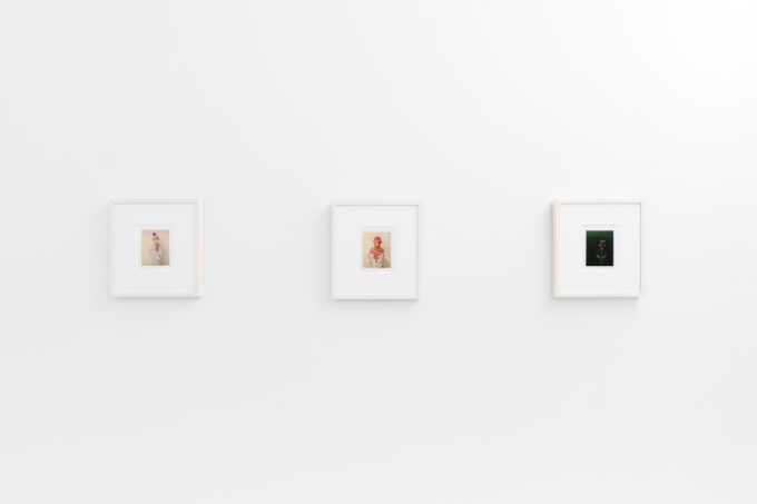 Small color photographs displayed on stark white gallery walls.