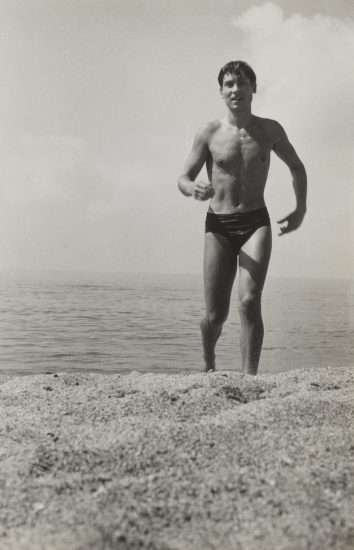 A black and white photograph of a man in a speedo walking out of the water.