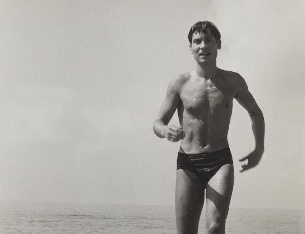 A black and white photograph of a man in a speedo walking out of the water.