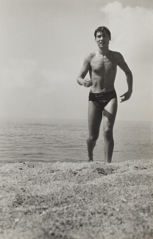 A black and white photograph of a man in a speedo walking out of the water.