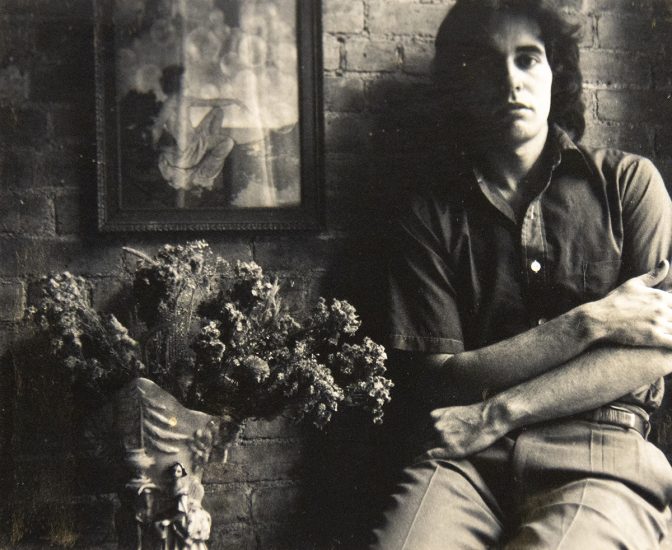 A black and white photograph of a young man with his arms crossed.