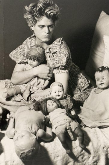 A black and white photograph of a boy in a gingham shirt with various toy dolls.